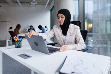 Data analyst in hijab closing laptop in end of working day at office
