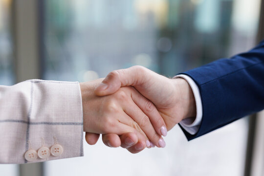 Anonymous man and woman in suits shaking hands at office 
