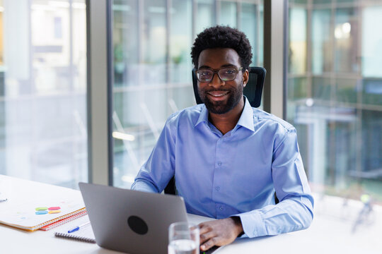 Bearded designer posing for photo while working on laptop in office