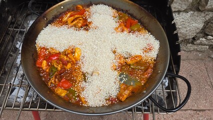 Traditional spanish paella preparation with vibrant vegetables and rice in a pan. Rice in the shape of a cross in paella. Typical cuisine of Spain. Stage of cooking paella. Ingredients for paella