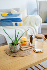 Homely atmosphere. Carafe of water, an aloe houseplant, an aroma diffuser, and a candle on a coffee table in the living room.