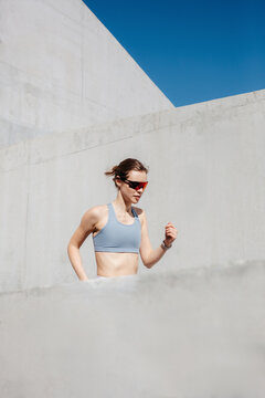 Fit woman runs up modern concrete stairs under bright blue sky