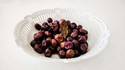 Marinated Black Olives with Bay Leaves in White Ceramic Bowl on White Background