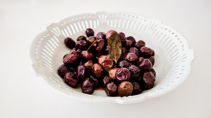 Marinated Black Olives with Bay Leaves in White Ceramic Bowl on White Background