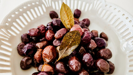 Marinated Black Olives with Bay Leaves in White Ceramic Bowl on White Background