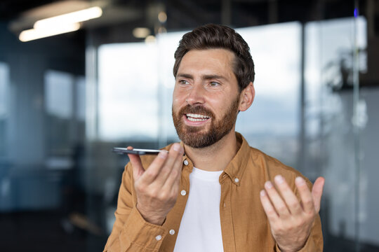 A professional man interacts with a smartphone, using its voice command feature, in an office environment with contemporary decor and natural lighting.