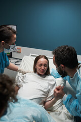Caucasian young adult woman lying in hospital bed experiencing labor pain, supported by medical...