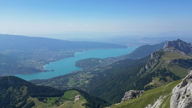 Drone aerial flyby of couple standing on cliff at La Tournette, overlooking Lake Annecy and French Alps, romantic mountain and lake panorama in summer travel destination