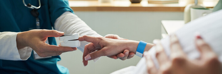 Caucasian female nurse placing pulse oximeter on finger of middle aged Caucasian woman patient lying in hospital bed, focusing on hands and medical procedure, healthcare concept