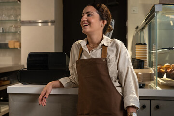 Young woman working as barista at cafe smiling and looking away