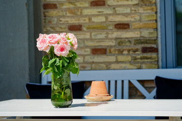 White table with glass vase of pink roses and ashtray nearby
