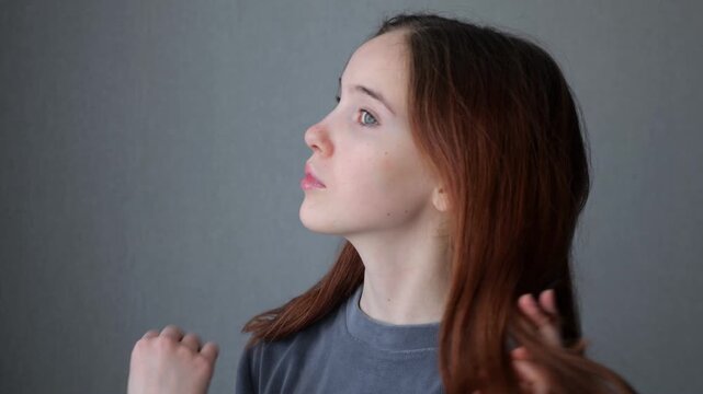 Teenager girl posing and touching hair on gray background