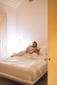 Mother Tucking Daughter into Bed in a White Peaceful Bedroom