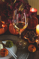Thanksgiving table setting with decorative pumpkins, candles and string lights on dark wooden table