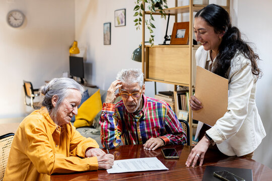 Senior couple meeting with financial advisor at home signing documents