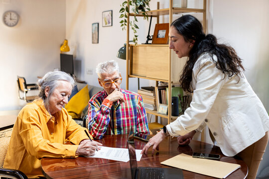 Senior couple meeting with financial advisor at home signing documents