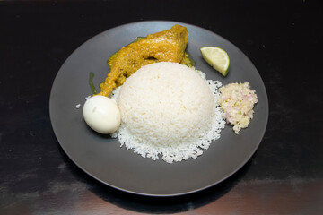 Asian rice plate with chicken curry, boiled egg, lime wedge, and onion salad on dark plate side view
