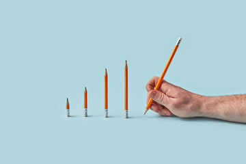 Hand writing with pencil beside rising pencil graph