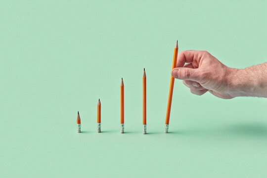 Hand holding pencil in rising bar graph of pencils on green