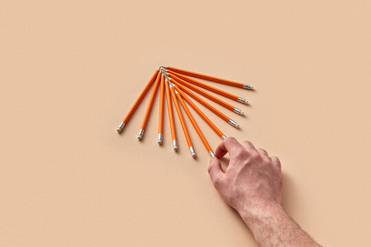 Hand arranging orange pencils on beige surface