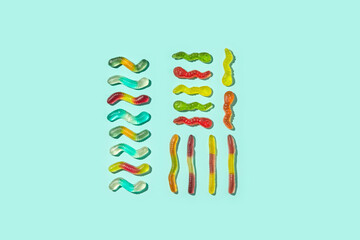 Assorted gummy worms lined up on cyan background