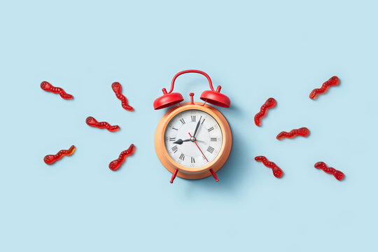 Red alarm clock with gummy worms on blue