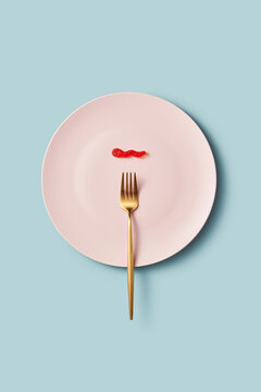Single red gummy worm on pink plate with fork