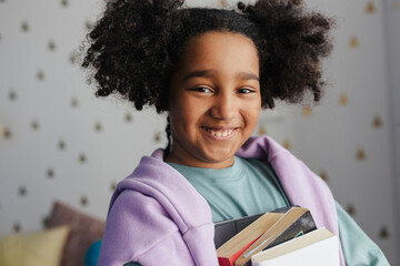 Black girl carrying books at home: education and learning concept