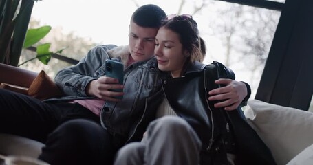 Young Couple Browsing Social Media on Phone, Enjoying Relaxing Time at Cafe - Powered by Adobe
