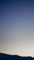 Crescent moon at sunset over mountain silhouette