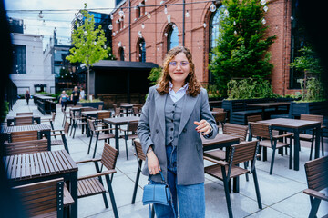 Turkish woman in gray blazer standing in urban outdoor cafe