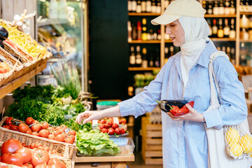 Woman in hijab picking tomatoes with vegetables in hand