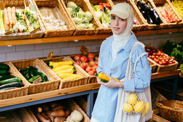 Woman in hijab holding yellow zucchini in grocery store