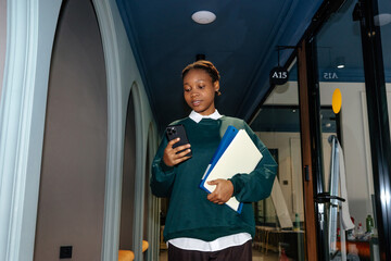 Female Employee in Office Hallway Holding Folders And Using Smartphone