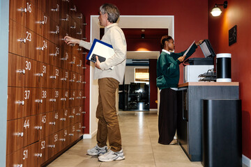 Man using locker while woman operating printer in coworking space