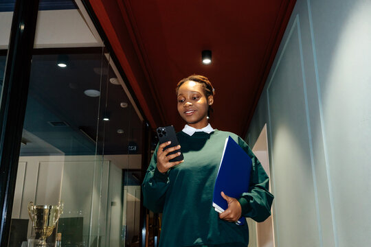 Smiling woman walking with folder and phone in office hallway
