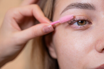 Caucasian woman brushing her eyelashes after lamination. 