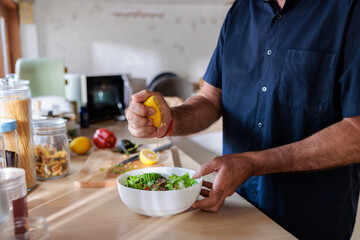 Man squeezing lemon juice onto salad in kitchen.