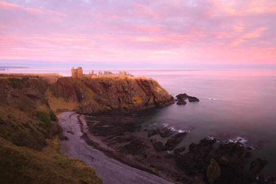 Dramatic colourful pink sunset at the historic medieval ruins of Dunnottar Castle on the Aberdeenshire coast in Scotland, UK.