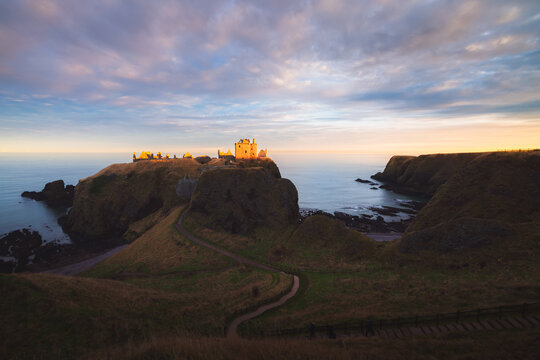 Dramatic golden light at sunset on the historic medieval ruins of Dunnottar Castle on the Aberdeenshire coast in Scotland, UK.