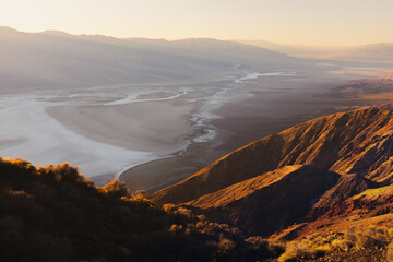 Golden beams of sunlight at sunset or sunrise over the desert landscape of Badwater Basin salt flats from Dantes View in Death Valley National Park, California, USA.