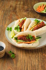 Step by step cooking of steamed bao buns stuffed with chicken, fresh cucumber and carrot on a wooden background. Ready bao buns stuffed with chicken and vegetables on a plate.