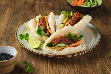 Step by step cooking of steamed bao buns stuffed with chicken, fresh cucumber and carrot on a wooden background. Ready bao buns stuffed with chicken and vegetables on a plate.