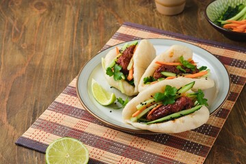 Step by step cooking of steamed bao buns stuffed with chicken, fresh cucumber and carrot on a wooden background. Ready bao buns stuffed with chicken and vegetables on a plate.