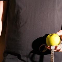 An obese man in a T-shirt shows his belly and apple in a hand
