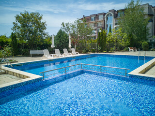 Clean outdoor pool with clear blue water, sun loungers, and umbrellas near modern apartment building. Peaceful summer vibe and relaxation area.