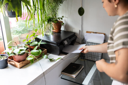 Woman picking up printed document from printer in green home office