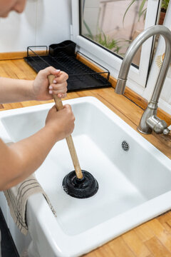 Woman using plunger to unclog kitchen sink drain