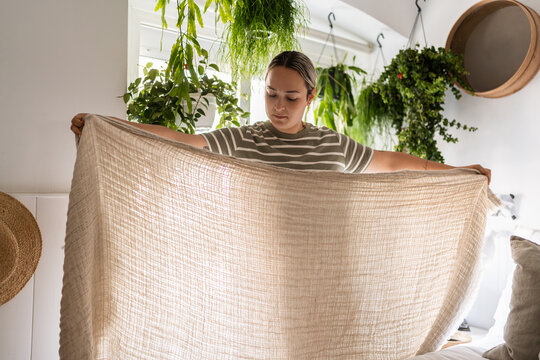 Woman holding blanket in front of plants in bedroom