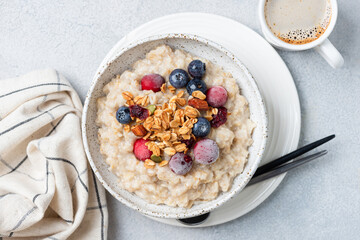 Oatmeal porridge bowl with frozen berries, granola topping and cup of coffee. Table top view. healthy breakfast meal